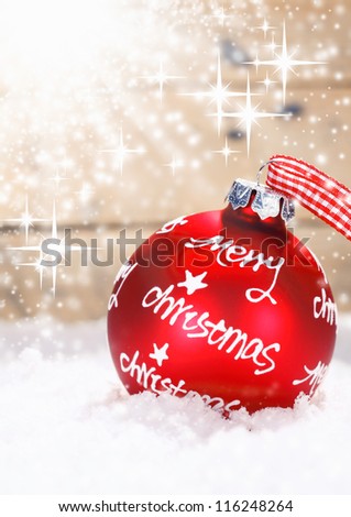 Red Merry Christmas bauble tied with a fresh red and white checked ribbon nestling in winter snow with twinkling stars of moisture lit by sun flare with copysapce