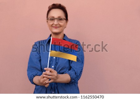 Armenia flag. Woman holding Armenian flag. Nice portrait of middle aged lady 40 50 years old with a national flag over pink wall background on the street outdoor.