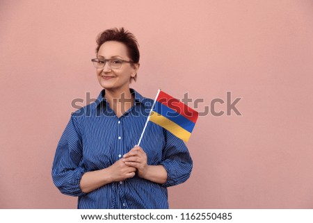 Armenia flag. Woman holding Armenian flag. Nice portrait of middle aged lady 40 50 years old with a national flag over pink wall background on the street outdoor.