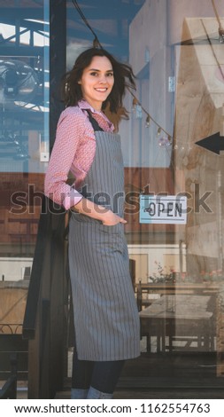 Beautiful mid 30s Caucasian female standing with an open sign near her small cafe, smiling and looking into camera. Small business concept