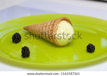 Ice cream in a waffle horn. Lying on a light green plate. Nearby lie a few berries of blackberries.