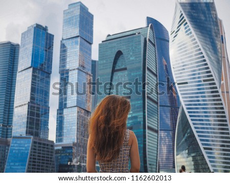 A woman with long hair stands with his back to the camera and looks at the high-rise buildings of the business center in Moscow
