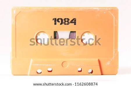 A vintage cassette tape from the 1980s era (obsolete music technology) labeled 1984 (my addition, not in the original image). Color: cream, sand. White background.

