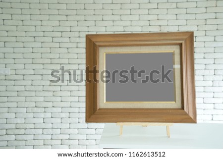 Wooden picture frame with empty blank grey space for your product montage, on table and white brick background.