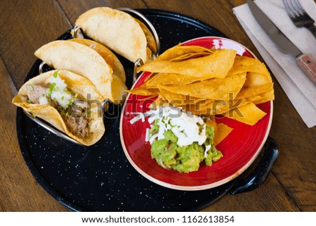 Traditional Mexican tacos with various fillings served with guacamole and nachos chips 

