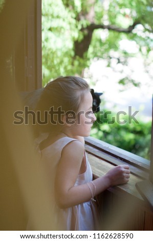little girl on the balcony with the cat, the child looks out the window, the girl and the black cat
