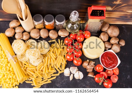 Uncooked raw macaroni, pasta and spaghetti next to fresh and healthy vegetables, variety of spices and sunflower oil on dark vintage rustic wooden background