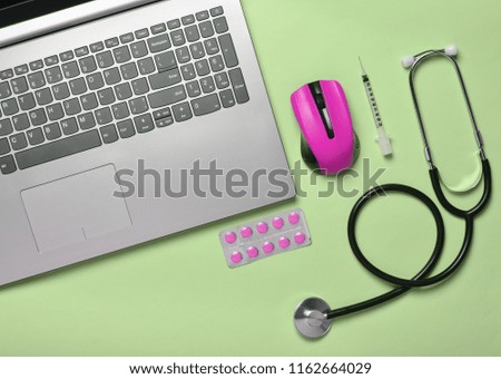 Workplace of a modern doctor. Laptop, wireless mouse, stethoscope, pills, syringe on green pastel background. Top view, minimalist trend

