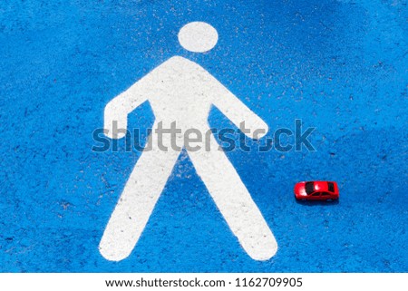 A red toy car hits the "pedestrian zone" sign on the ground/pavement/sidewalk. The sign is white and the asphalt is blue. Concept of traffic safety. Violation of traffic rules.