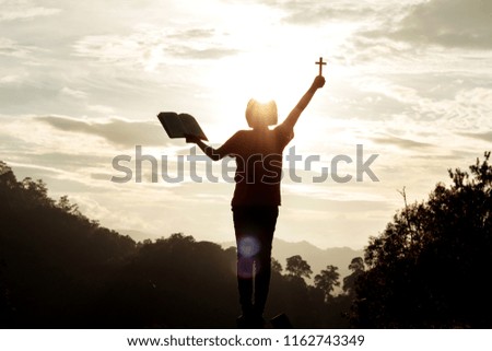 silhouette human praying to the GOD while holding a crucifix symbol with bright sunbeam on the sky