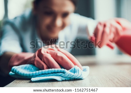 Young Smiling Woman in Gloves Cleaning House. Closeup of Happy Beautiful Girl wearing Protective Gloves Cleaning Desk by spraying Cleaning Products and wiping with Sponge. Woman Cleaning Apartment Royalty-Free Stock Photo #1162751467