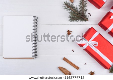 Top view of blank notebook on white wooden background with xmas decorations, copy space. Christmas background with notebook for wish list or to do list, red gift boxes, fir tree branches. Flat lay