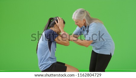 Old female paramedic examining soccer player's injury on green screen