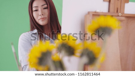 A young asian woman painting sunflowers in the foreground on green screen
