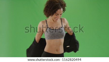 Young fit black girl in sports bra takes her jacket off on green screen