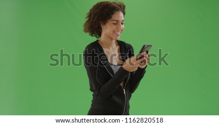 Young african American girl in workout attire uses smart phone on green screen