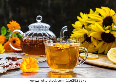 Tea with marigold and dog rose on a dark wooden background.