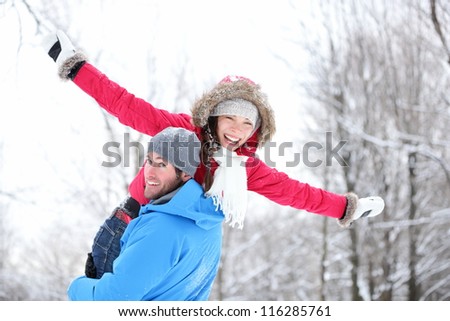 Winter fun couple playful together during winter holidays vacation outside in snow forest. Happy young interracial couple, Asian woman, Caucasian man.