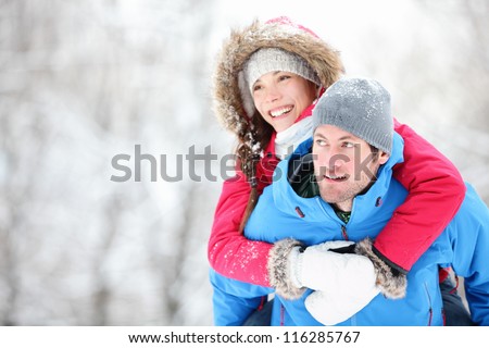 Happy winter travel couple. Man giving woman piggyback ride on winter vacation in snowy forest. Young interracial couple, Asian woman, Caucasian man.