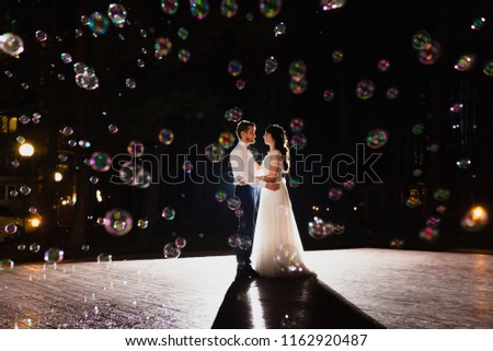 Couple of newlyweds dancing wedding dance in the darkness and huge amount of soap bubbles are flying in the air