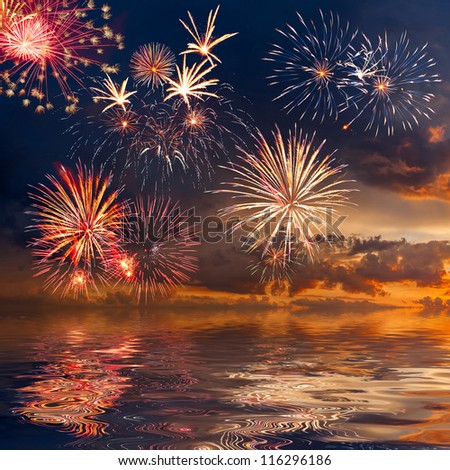Beautiful colorful holiday fireworks in the evening sky with reflection and majestic clouds, long exposure