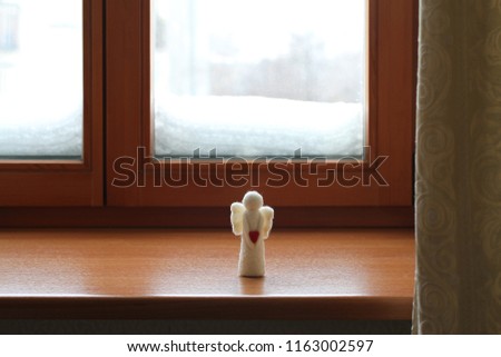 Woolen toy angel standing on a windowsill against a snowy window