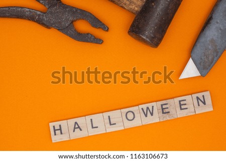 From the wooden squares is composed the word halloween and lies on an orange background next to a knife, pliers and a hammer