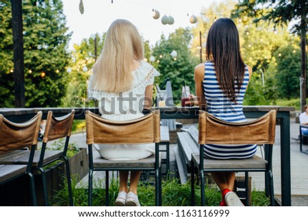 Сlose up, back view picture of two women relaxing on party making cheers by their summer cold tasty cocktails, vacation fun mood. Focus on glasses.