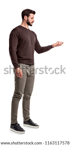 A young man in fashionable casual closes stands in a side view and looks at one hand turned up as if holding something. New product. Exclusive offer. One time chance. Royalty-Free Stock Photo #1163117578