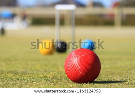 In the foreground is a red croquet ball on a green croquet lawn in Australia with a defocused croquet hoop and balls in the background Royalty-Free Stock Photo #1163124958