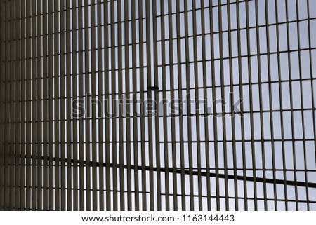 Close up outdoor perspective view of an iron grid with blue sky in background. Pattern of rectangular shapes with crossing lines. Textured surface. Abstract geometric picture of a metallic structure. 