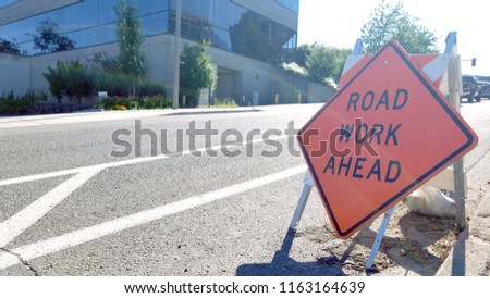 Road Work Ahead sign by the road under bright sunny day