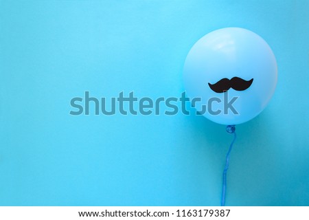 Hand holding blue balloon with a paper mustache on blue paper background. Cut out style. Father's day or mustache day concept. Top view. Flat lay. Copy space Royalty-Free Stock Photo #1163179387