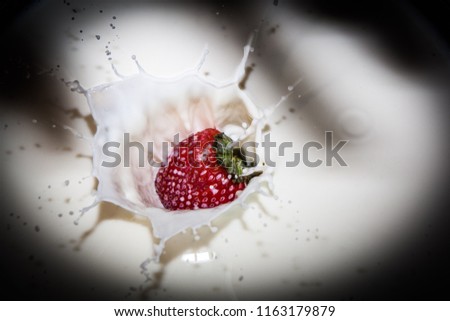 A strawberry makes a splash in to a bowl of milk after being dropped from height with the shadow of the hand that dropped the strawberry on the surface of the milk 