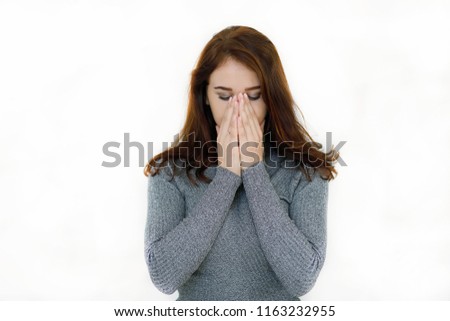 Emotional portrait of tired and cold-haired dark-haired young woman in gray sweater covering her nose with her hands while sneezing isolated on white background. Lifestyle concept. Medicine