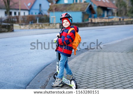Healthy little preschool kid boy riding on scooter riding to school or preschool. children activities outdoor in winter, spring or autumn. funny happy child in colorful fashion clothes and with helmet