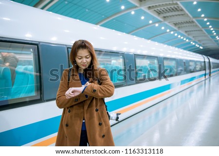 Young asian woman looking her watch while checking time for the train at railway station.