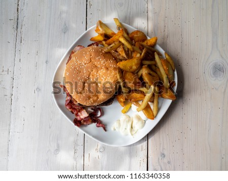 Big cheese burger with vegetables, bacon and sauce. Served on a plate on a white wood table - Pictured from above/top