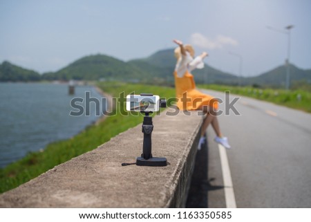 Young asian woman wearing yellow dress with camera standing on a dam and selfie a photo enjoy sunrise in the morning at  Bang Pra Dam Chonburi Thailand.