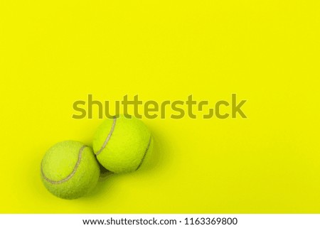 A flat lay photo of two yellow tennis balls on the bright yellow background. 