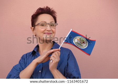 Belize flag. Woman holding Belize flag. Nice portrait of middle aged lady 40 50 years old with a national flag over pink wall background outdoors.