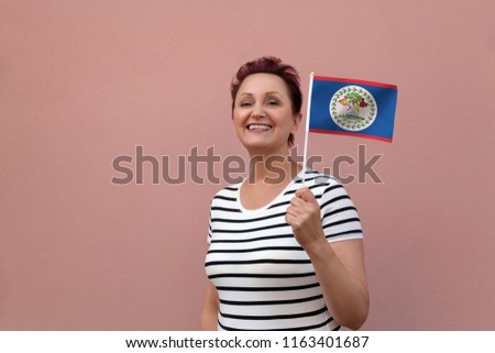Belize flag. Woman holding Belize flag. Nice portrait of middle aged lady 40 50 years old with a national flag over pink wall background outdoors.