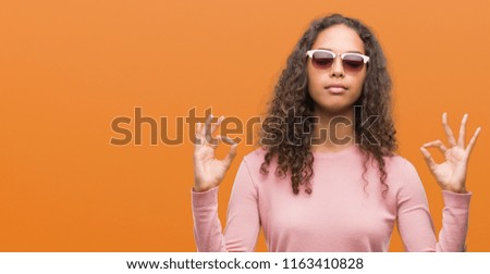 Beautiful young hispanic woman wearing sunglasses relax and smiling with eyes closed doing meditation gesture with fingers. Yoga concept.