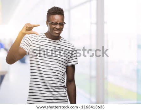 Young african american man wearing glasses and navy t-shirt smiling and confident gesturing with hand doing size sign with fingers while looking and the camera. Measure concept.