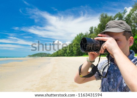 Traveler takes a photo with a DSLR camera on Suan Soan Pradipat beach near Hua Hin, Thailand. Beautiful landscape (blurred) with forest and blue sky is behind him.