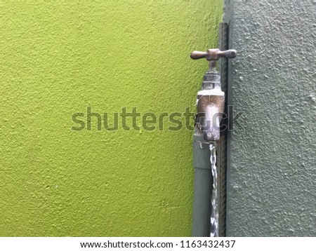 Drain water from the tap metal outdoor over green colored concrete wall background.