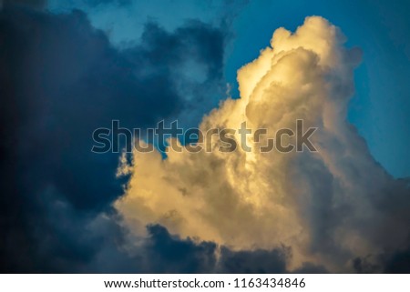 Dark cloud beginning to obscure tall cumulus cloud on a summer evening, for themes of weather and uncertainty, change, transition