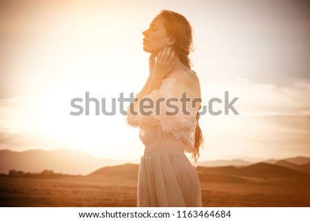 red-haired girl in a field of wheat in a white dress smiles a lovely smile , a perfect picture for advertising in the style lifestyle. beautiful cinematographic picture at sunset