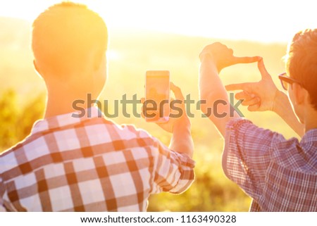 two men take pictures of the sunset on the phone in the sun