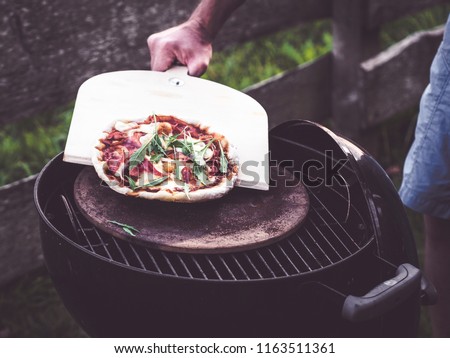using a pizza shovel to transfer the homemade grilled pizza from hot pizza stone